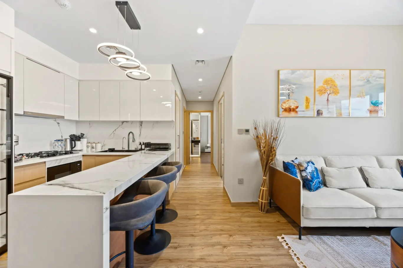 Open-plan kitchen with white cabinets, marble island, and a beige sectional sofa in the living area.