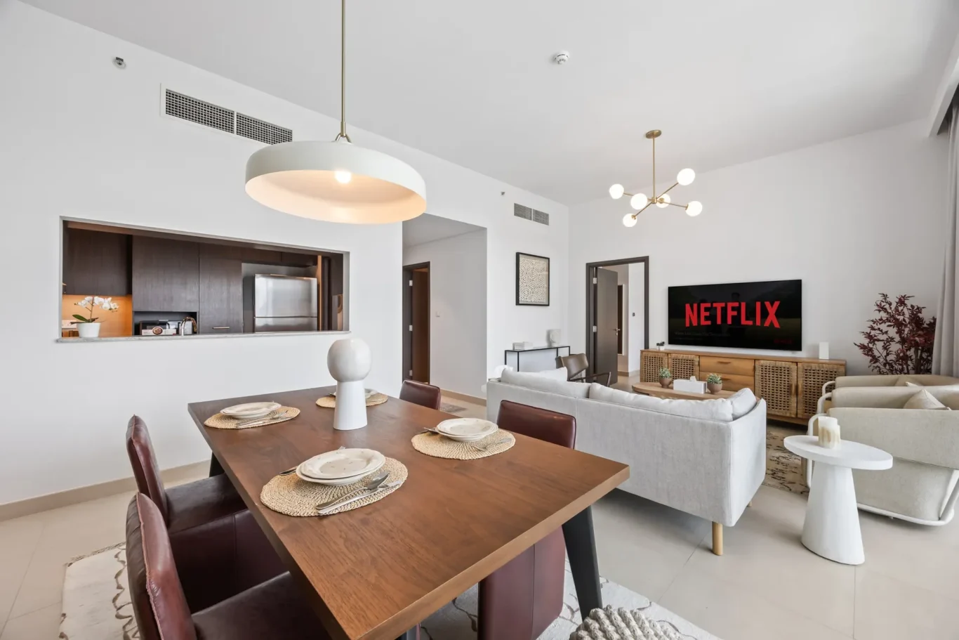 Open-plan living and dining room with a wooden table set for six, grey sofas, and a Netflix screen.
