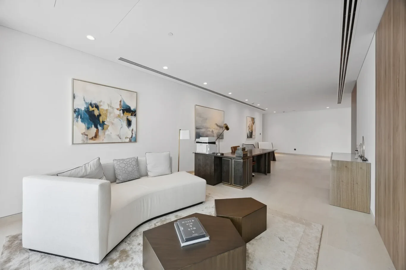 Bright contemporary living room with a white curved sofa, abstract wall art, and a dark wooden coffee table set on a light rug.