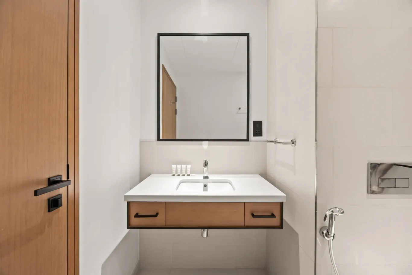 Modern bathroom vanity with white countertop, wooden drawers, and a black-framed mirror above.