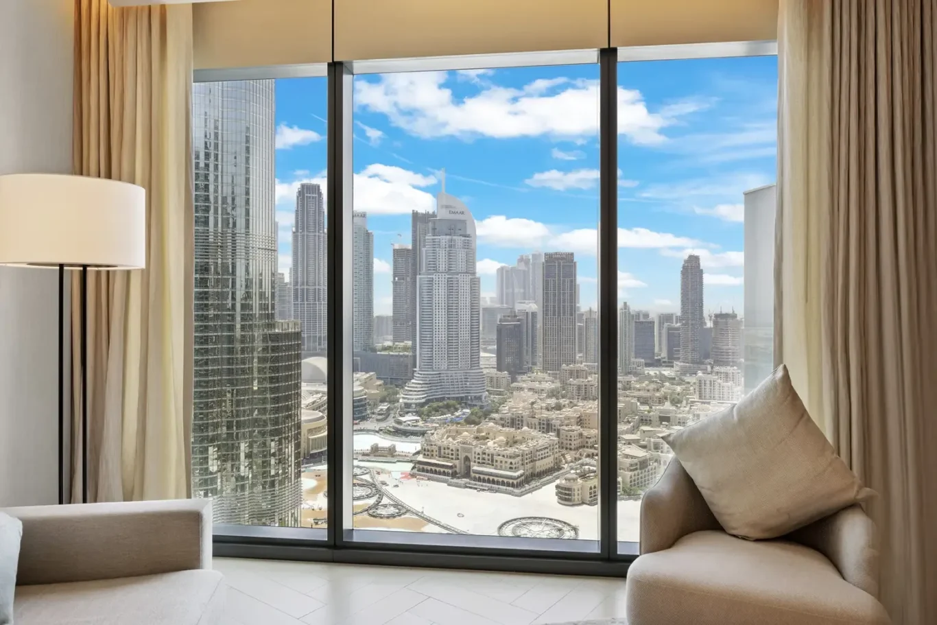 Hotel living area with a floor-to-ceiling window showing a city skyline of tall glass skyscrapers under a blue sky.