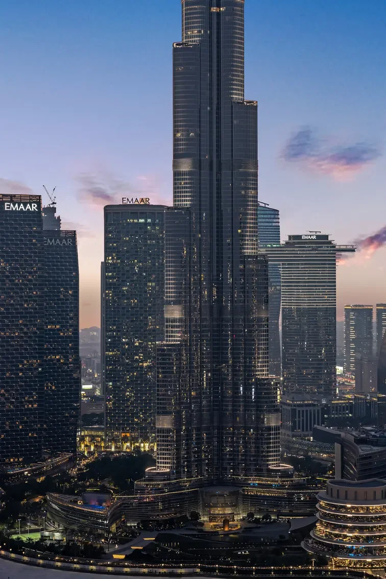 Dubai skyline at dusk with the tall central Burj Khalifa flanked by illuminated glass skyscrapers bearing Emaar logos