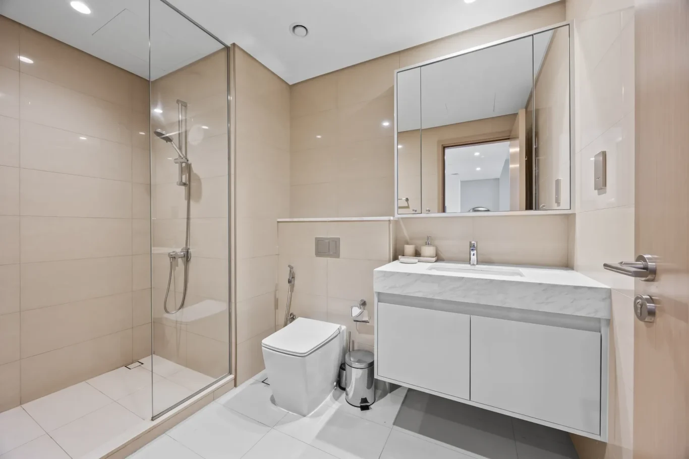 Modern beige-tiled bathroom with a glass-enclosed shower, wall-mounted marble vanity, and white toilet.—informative view of a contemporary bathroom setup