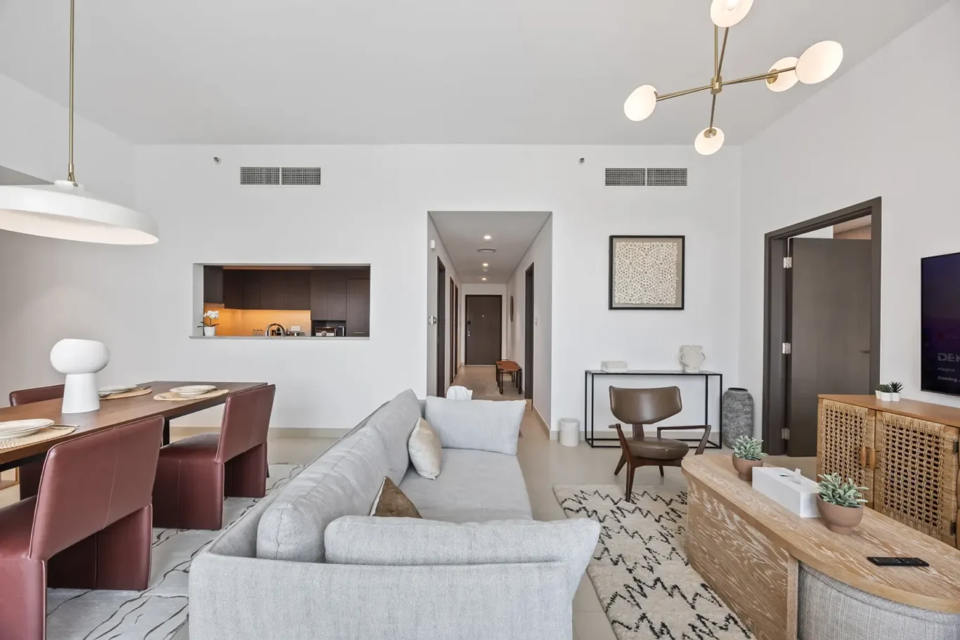 Open-concept living and dining area with a gray sofa, brown dining chairs, and a brass chandelier in a bright modern home.