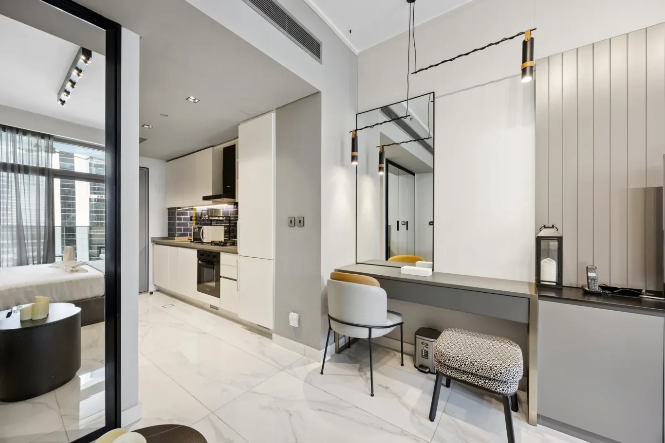 Open-concept living space showing a white-kitchen area, a long gray counter, and a dining desk with mirrors and pendant lights.