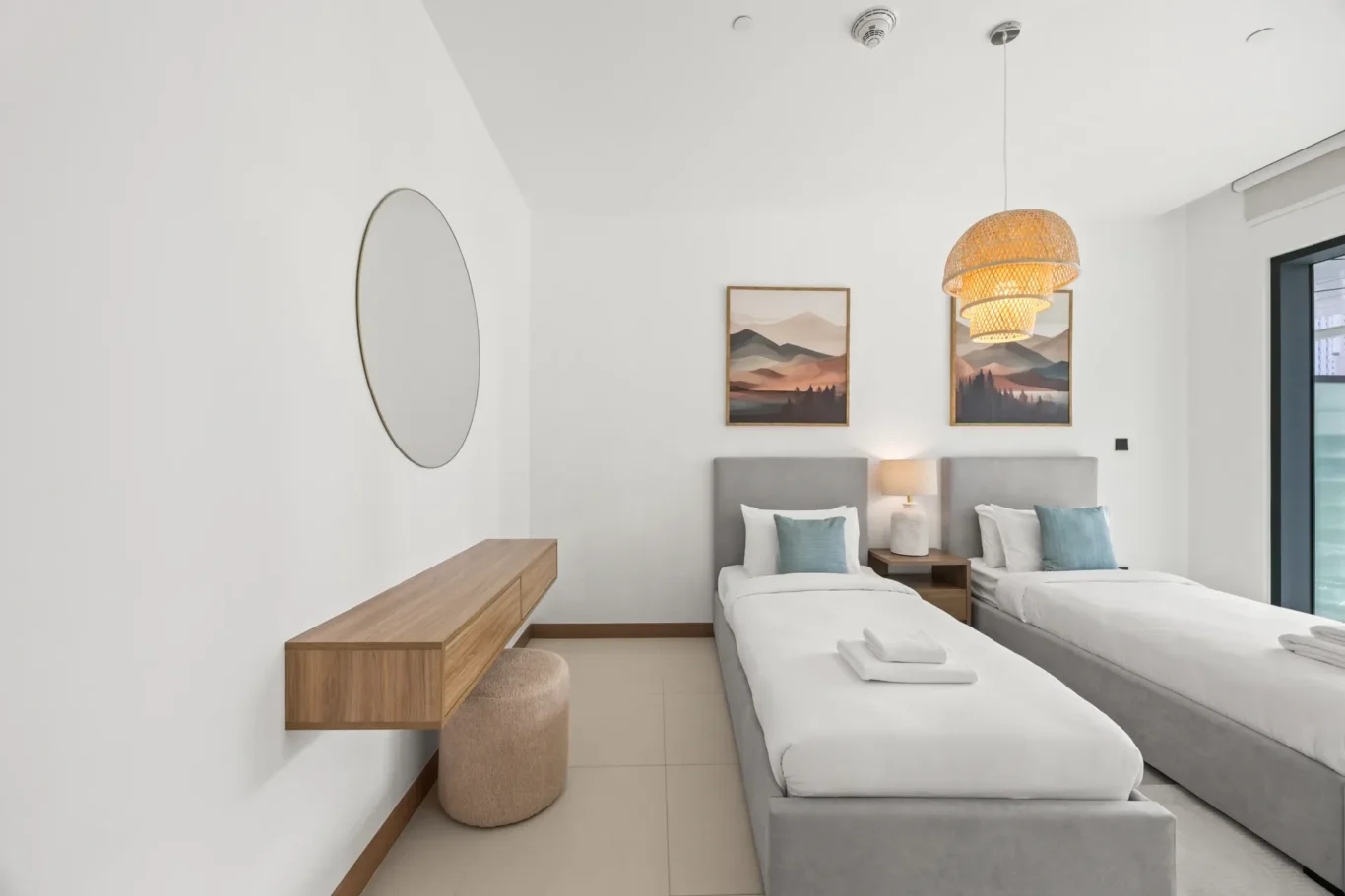 Hotel room with two twin beds, light gray headboards, and a woven pendant lamp hanging from the ceiling.