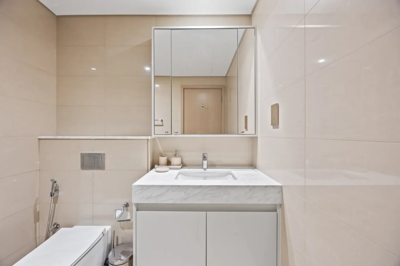 Modern beige-tiled bathroom with a marble sink counter, mirrored cabinet, and chrome fixtures.