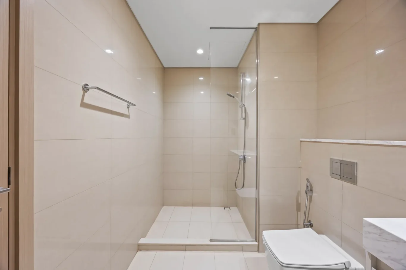 Modern bathroom with a glass shower enclosure, beige wall tiles, and a wall-mounted toilet.