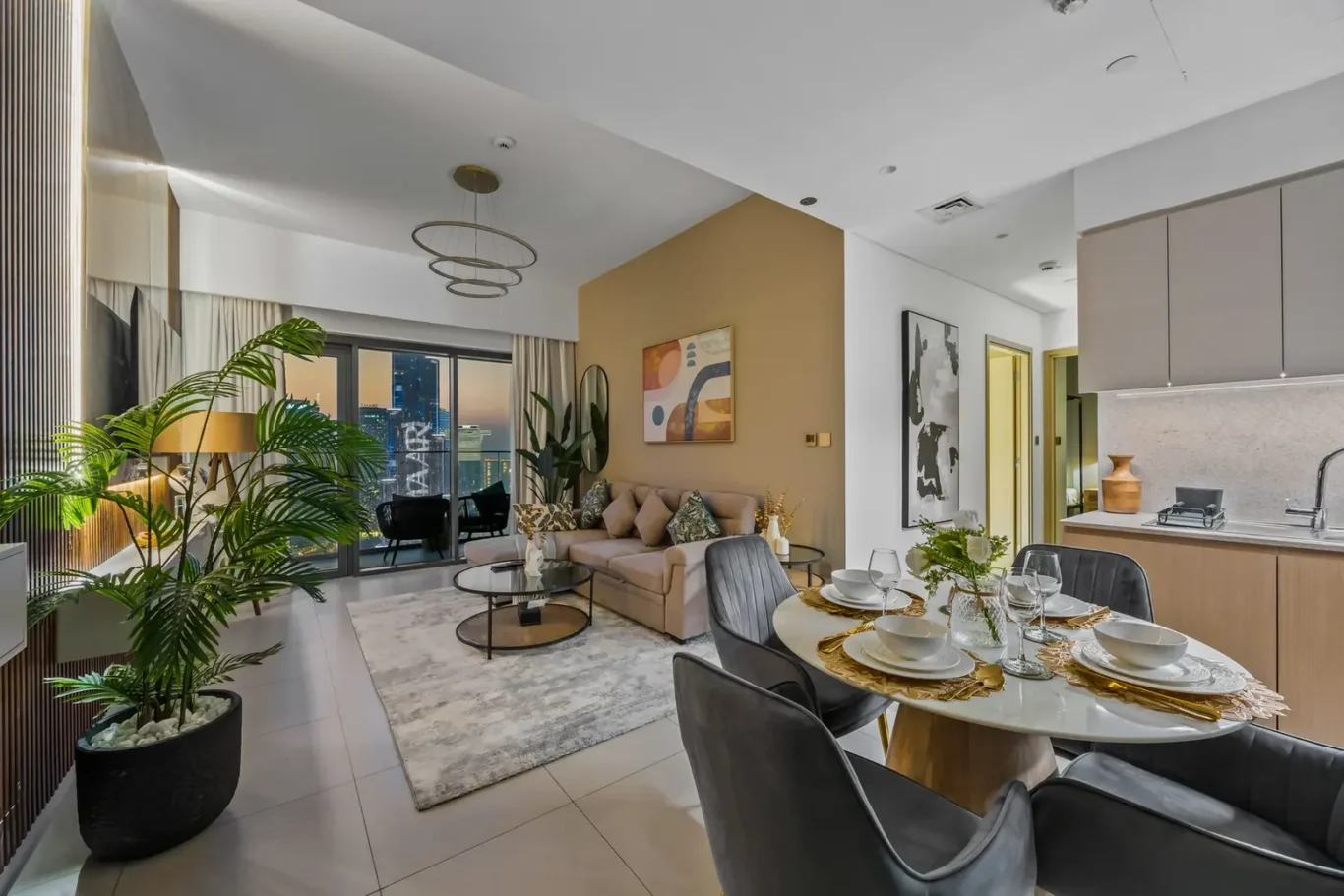 Open-plan living and dining area in a high-rise apartment with a city skyline view, beige sofa, and indoor plants.