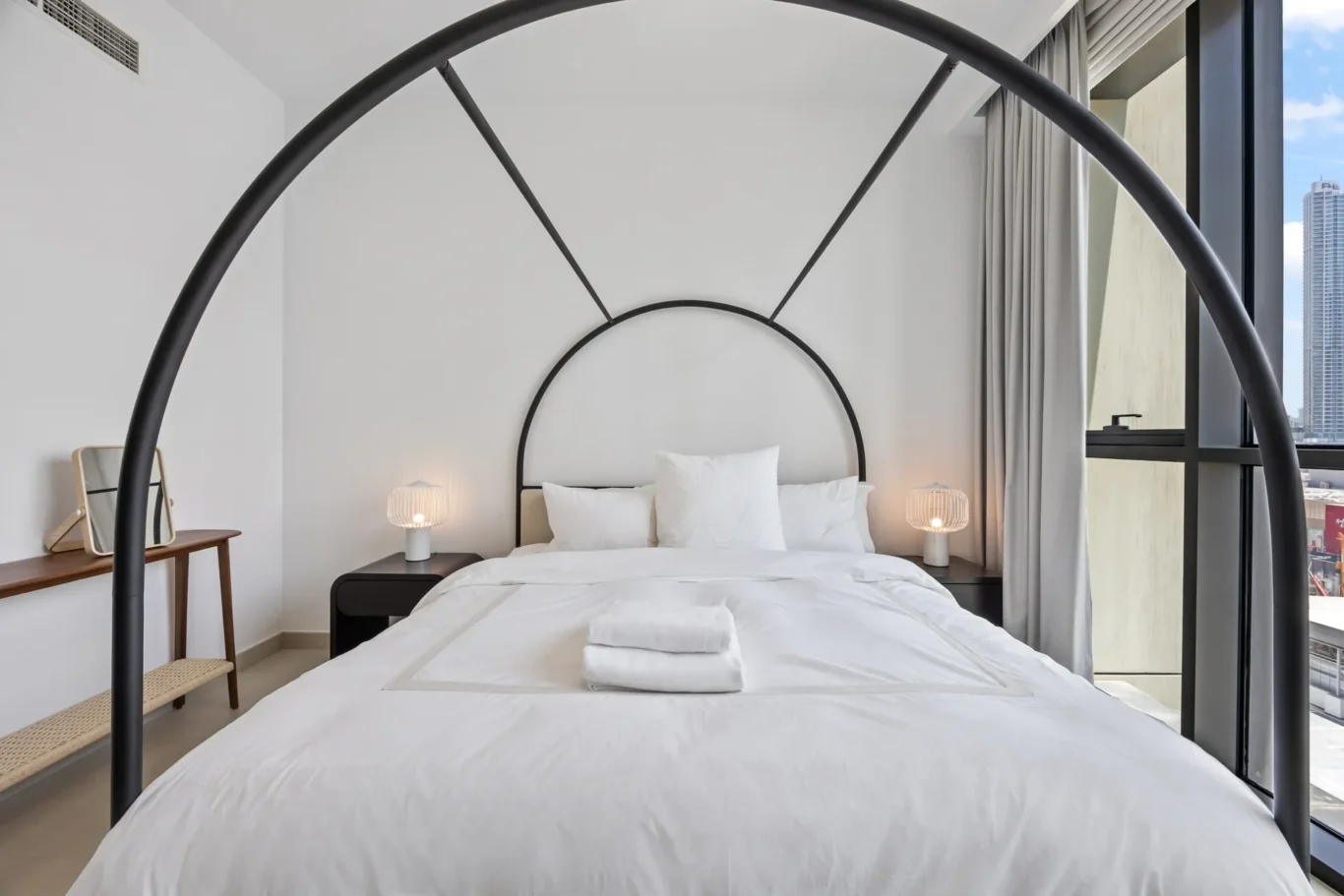 Minimalist bedroom with a black metal arched bed frame, white bedding, and soft bedside lamps on dark nightstands.