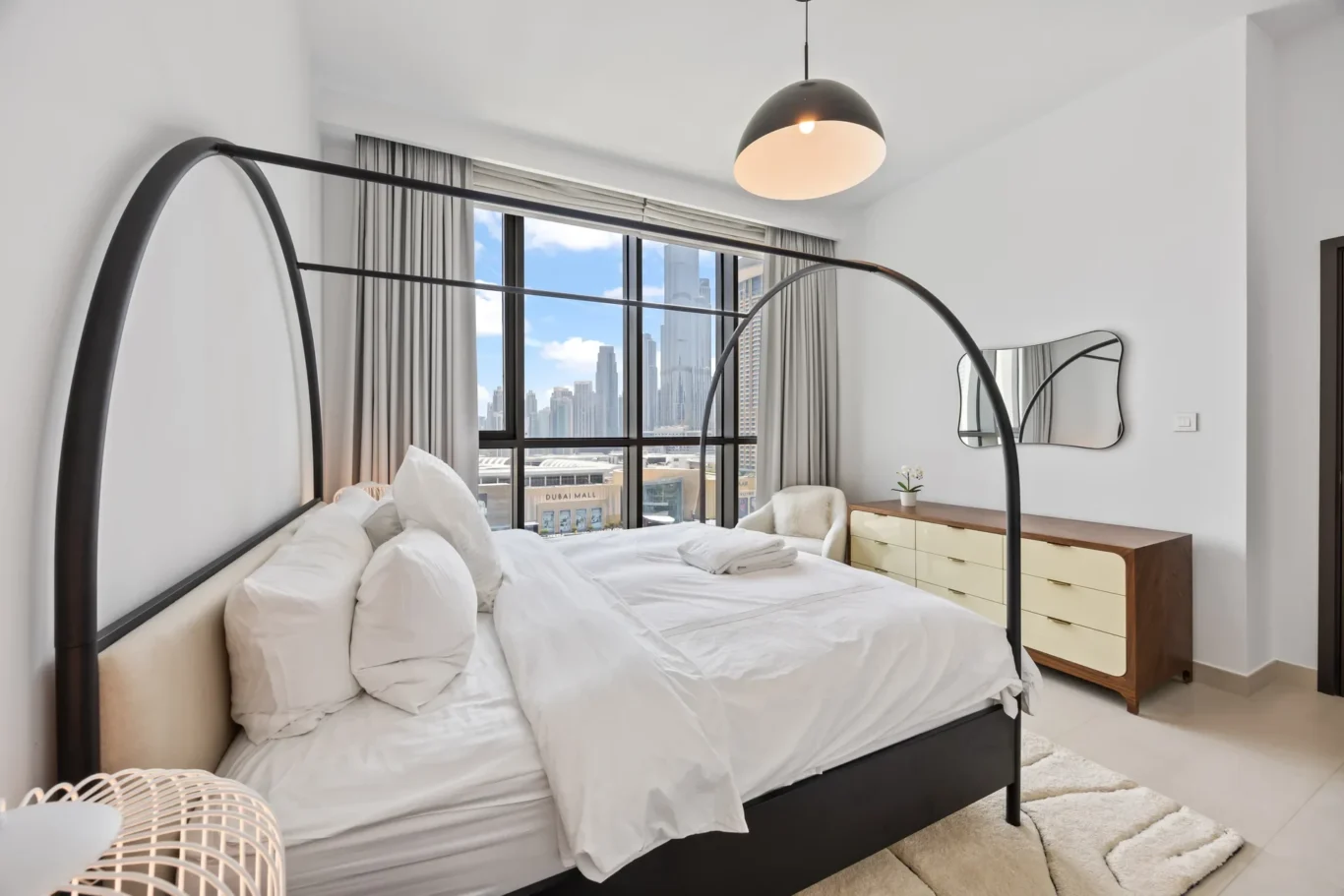 Modern bedroom with a black metal four-poster bed, white bedding, and a large window showing a city skyline.