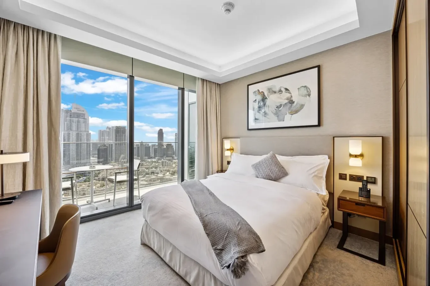 Hotel room with a king bed, abstract painting, and a balcony overlooking a city skyline.