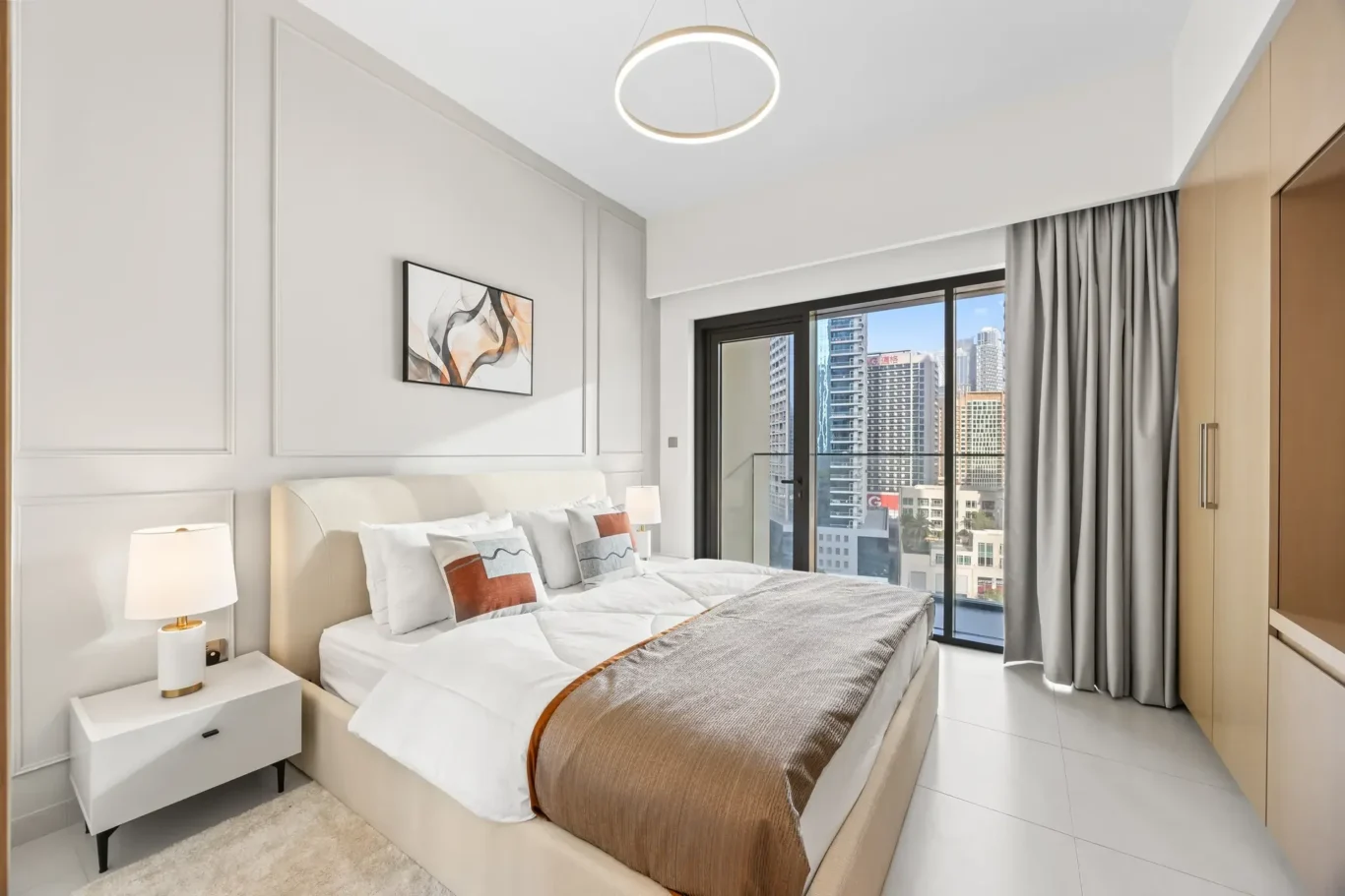 Modern hotel bedroom with a large bed, white linens, brown bed runner, two nightstands, circular ceiling light, and city view through glass doors.
