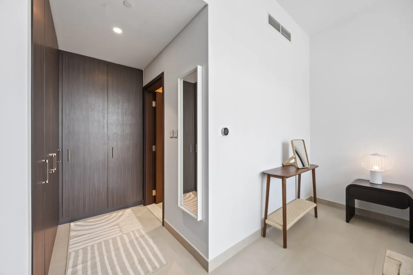 Entryway with tall dark wood closets on the left, a wall mirror on the right, and a small wooden table with a mirror nearby.