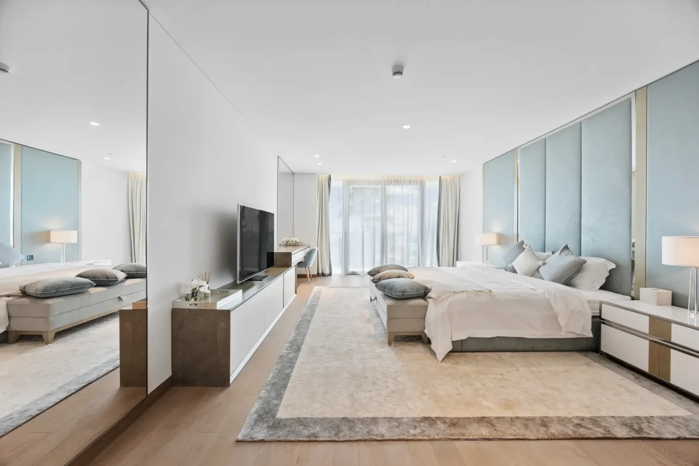 Luxurious modern hotel suite with two beds, light gray bedding, and a flat-screen TV opposite a mirrored wall.