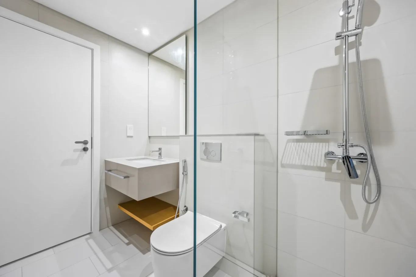 Modern white bathroom with a glass shower partition, wall-mounted sink, and wall-hung toilet in a minimalist design.