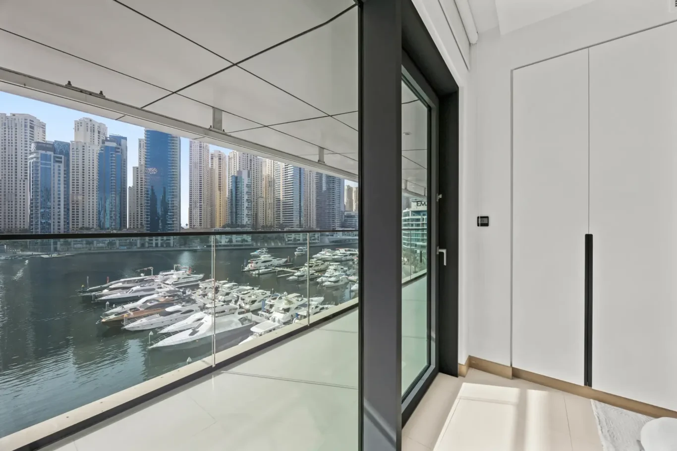 Modern balcony with a glass railing overlooking a marina and a cluster of high-rise buildings across the water.