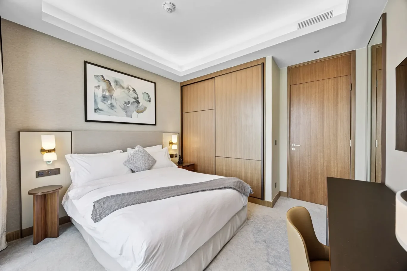 Hotel bedroom with a king bed, white linens, gray throw, and a large abstract framed artwork above the headboard.