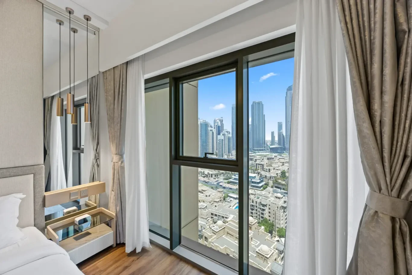 Hotel room with large window showing city skyline; sheer white and beige curtains frame the view.