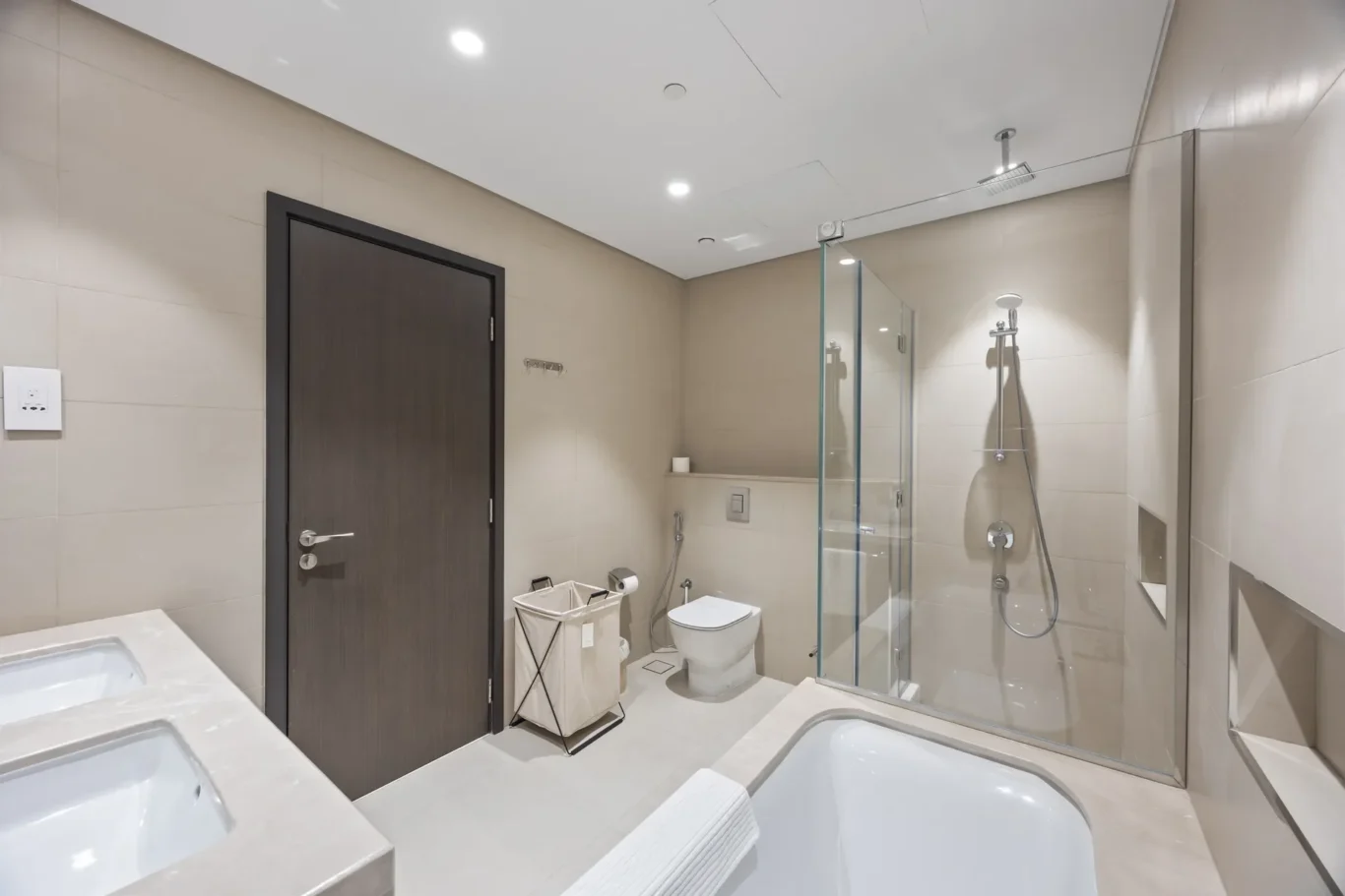 Modern bathroom with two sinks, a dark wooden door, a toilet, and a glass-walled shower.