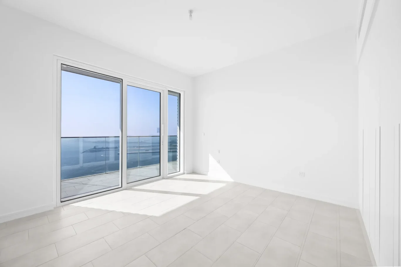 Bright, empty room with large sliding glass doors opening to a balcony overlooking the ocean.