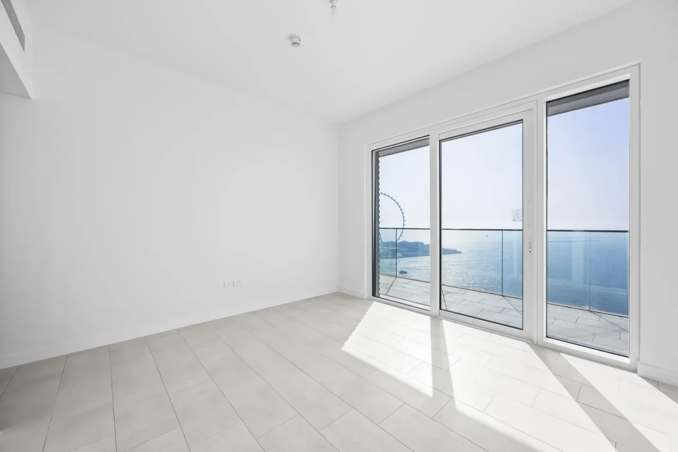 Empty white room with large sliding glass doors opening to a balcony and a sea view.