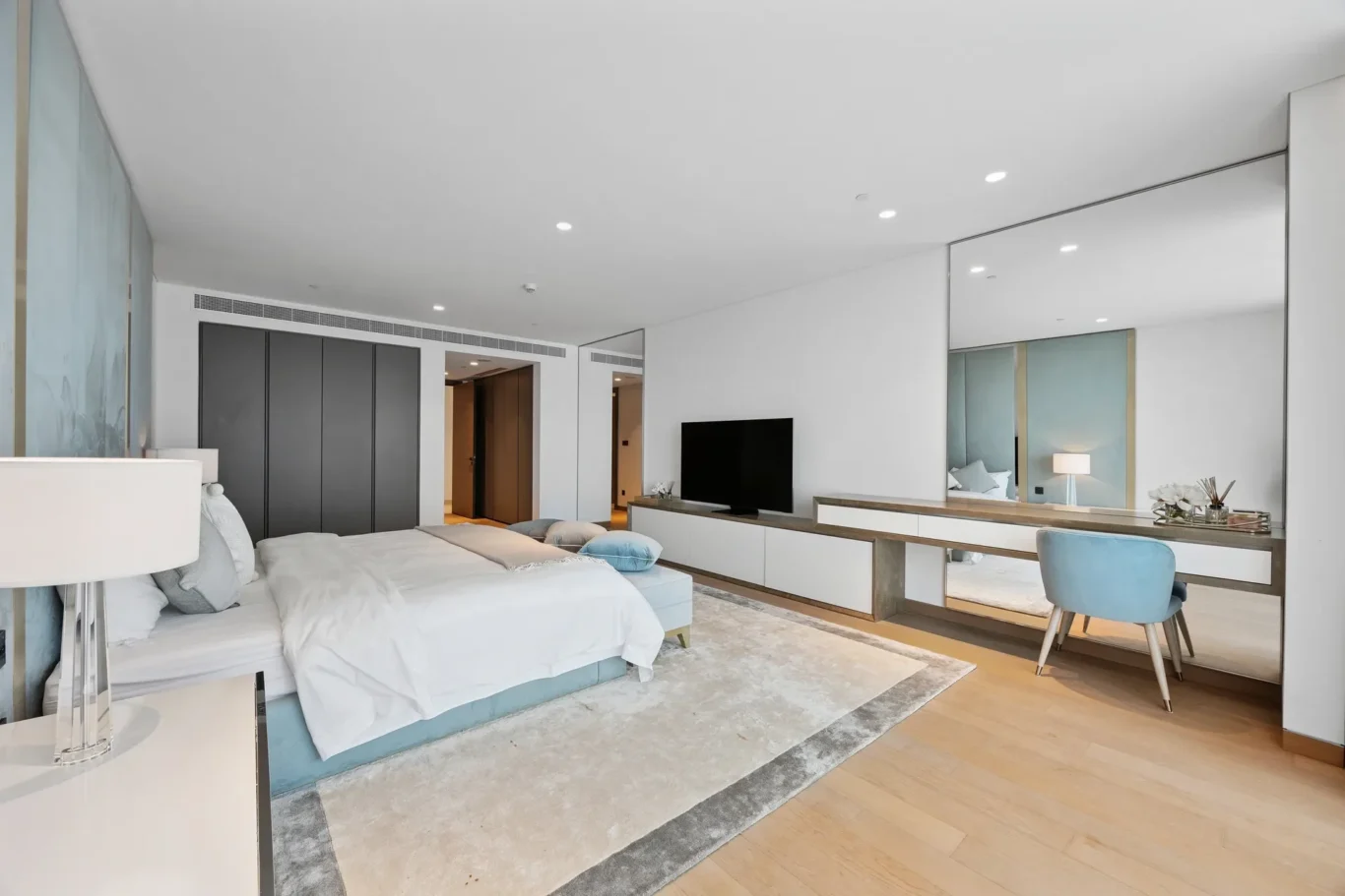 Spacious, modern hotel room with two beds, a long media console, and a wall of mirrors opposite a seating area.