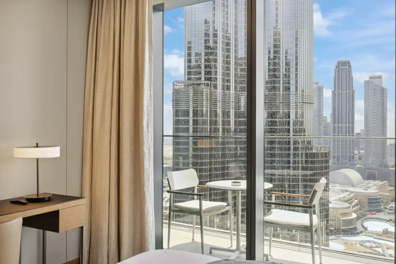 Hotel room interior with a balcony and a city skyline of tall glass skyscrapers outside the window.
