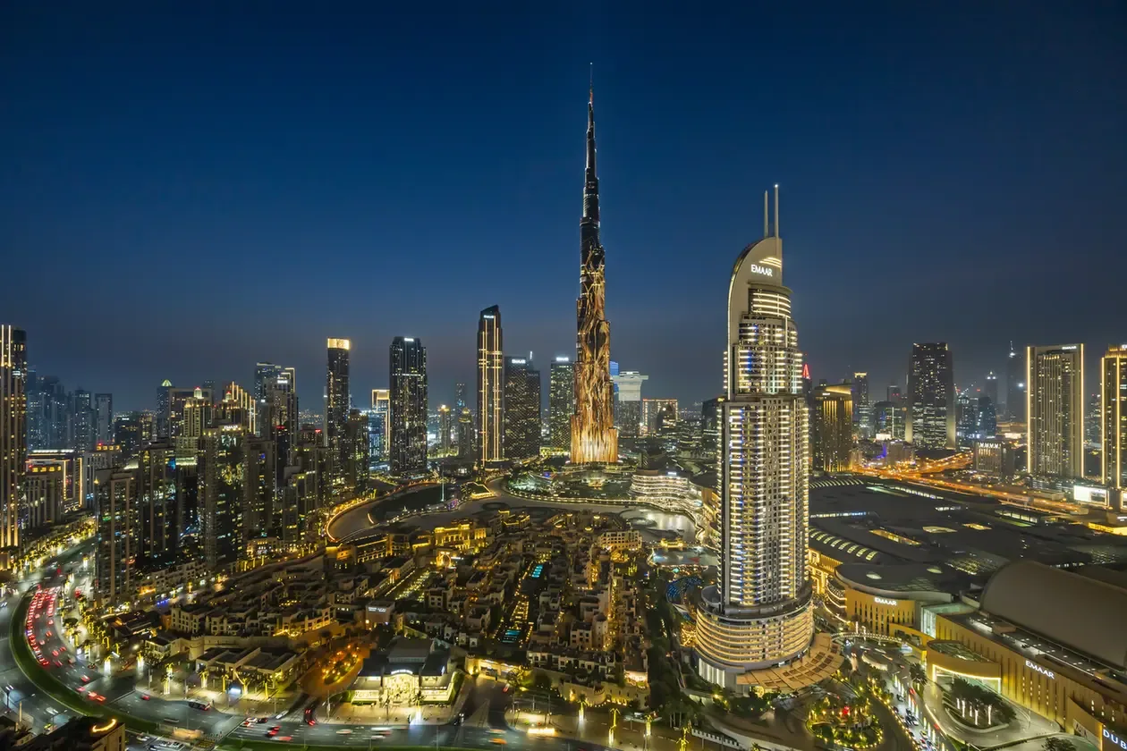 Night aerial view of Dubai's skyline, centered on the Burj Khalifa with illuminated streets and buildings.