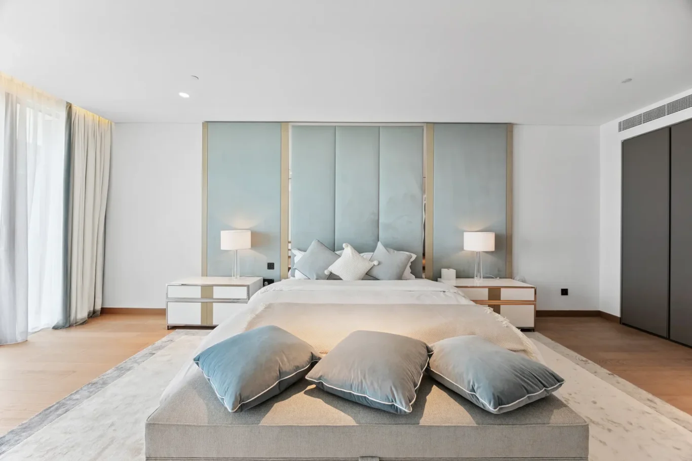 Hotel bedroom with a king-size bed, pale blue upholstered headboard panels, and twin nightstands with lamps.