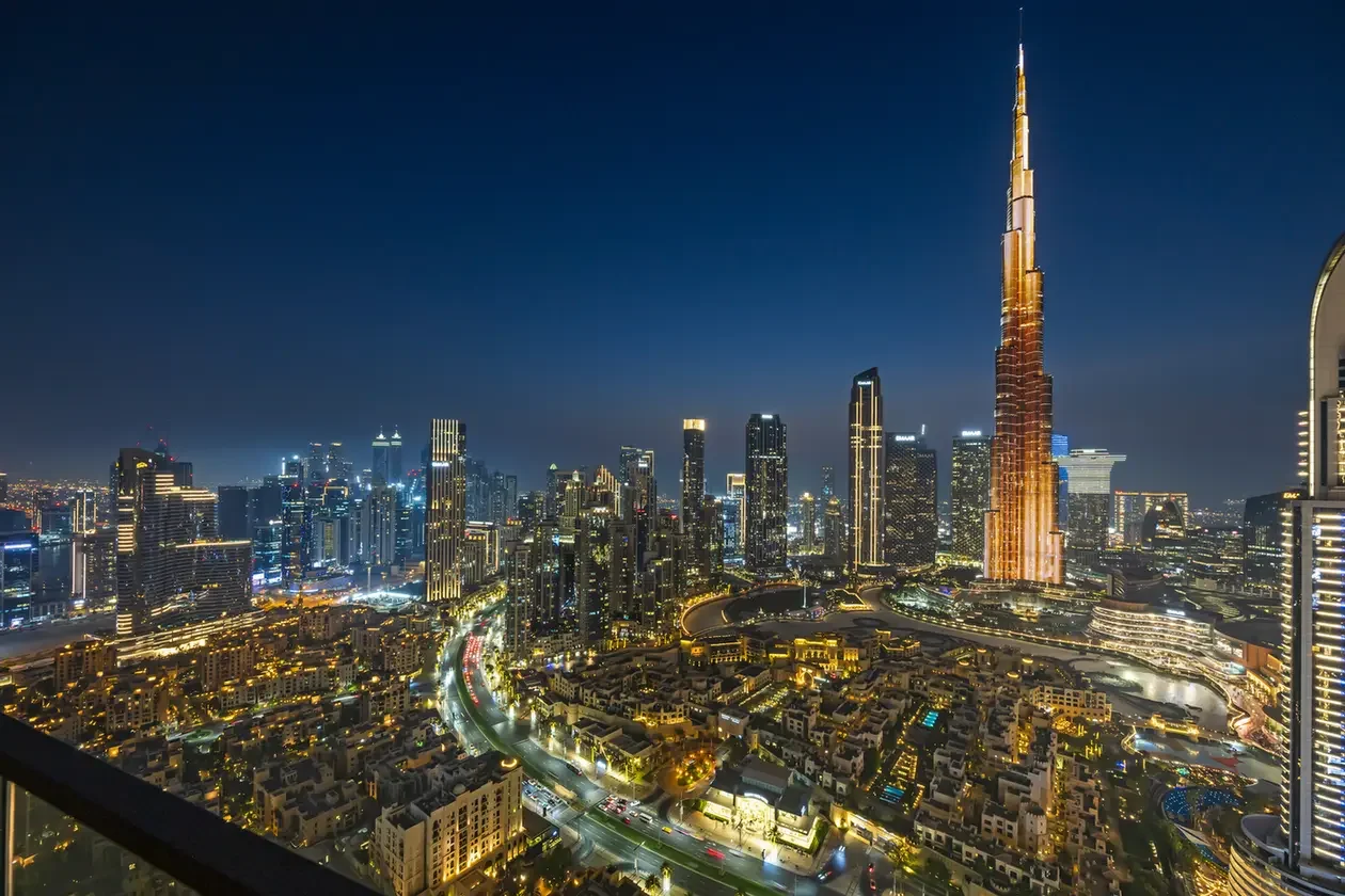 Nighttime aerial view of Dubai's skyline with illuminated skyscrapers, dominated by the tall Burj Khalifa.