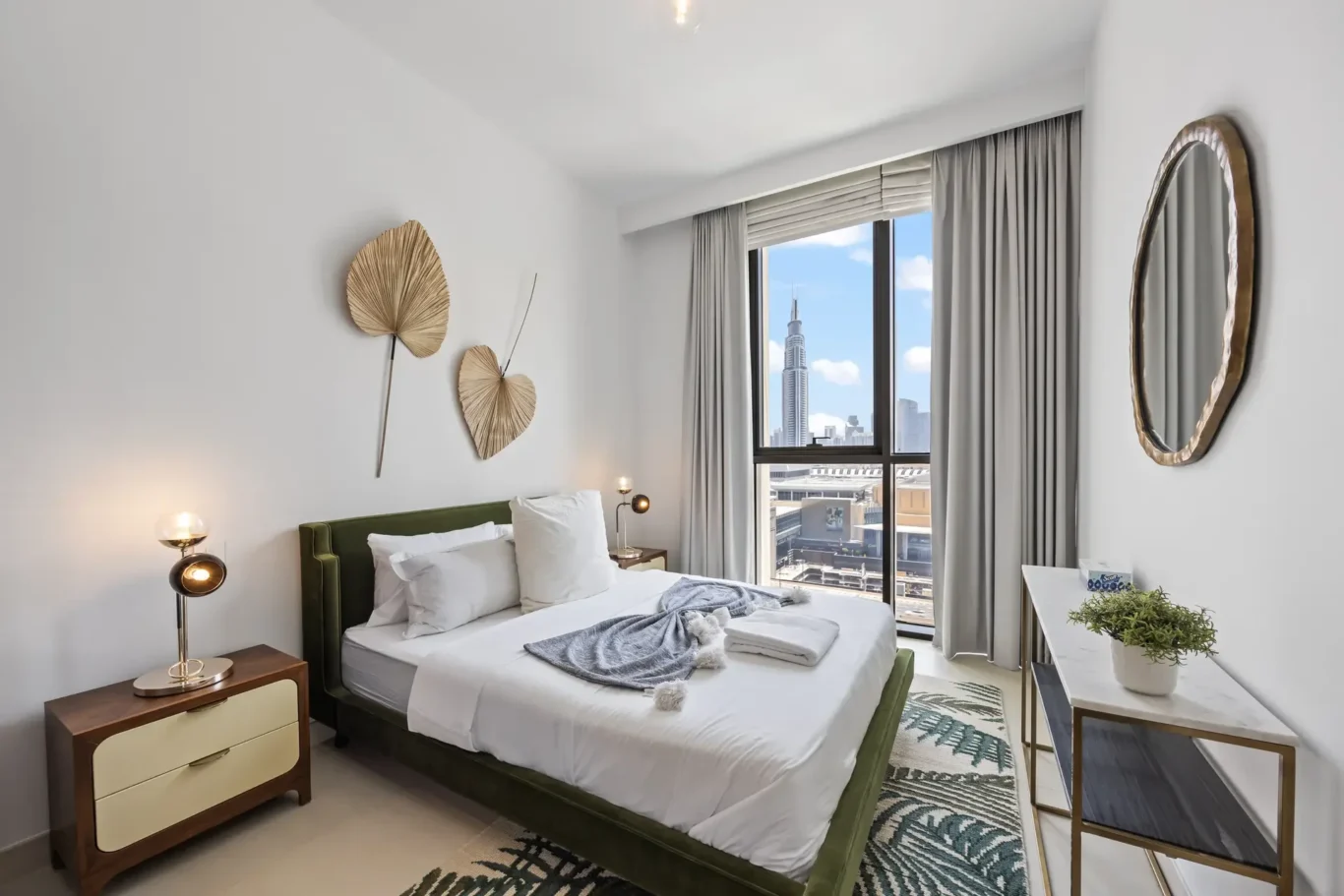 Cozy modern bedroom with a green upholstered bed, white bedding, and decorative wall fans, near a window with city view.