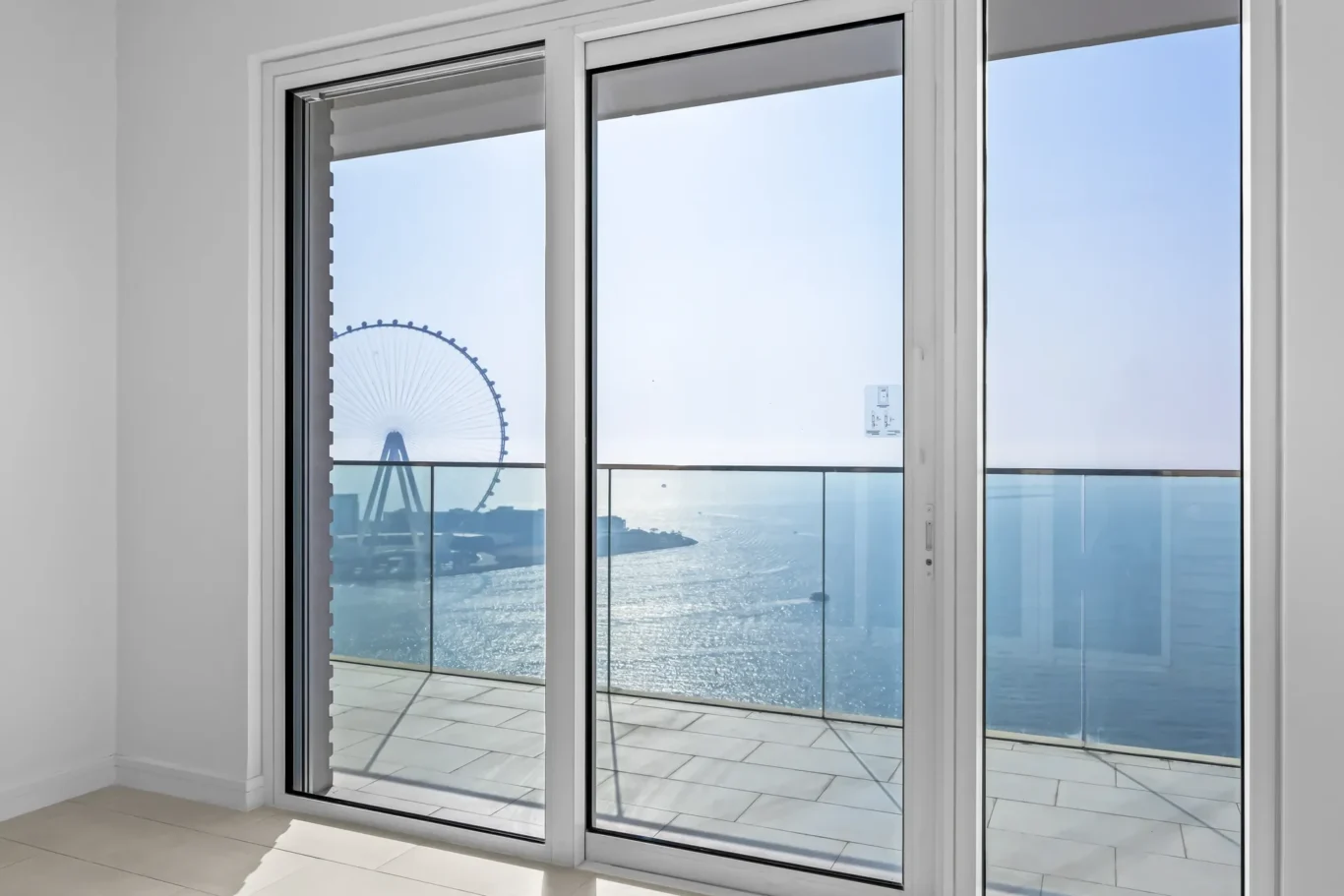 Sliding glass doors open to a balcony with a waterfront view and a distant Ferris wheel outside.