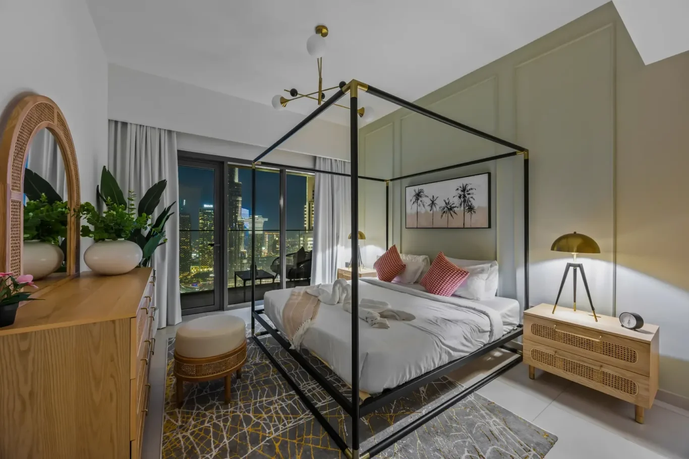 Modern bedroom with a black metal four-poster bed, beige bedding, red throw pillows, and a city skyline view through large windows.”,
