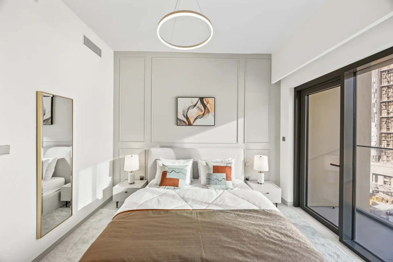 Modern hotel-style bedroom with a large glass door to a balcony, white walls, and a king bed with neutral bedding and accent pillows.