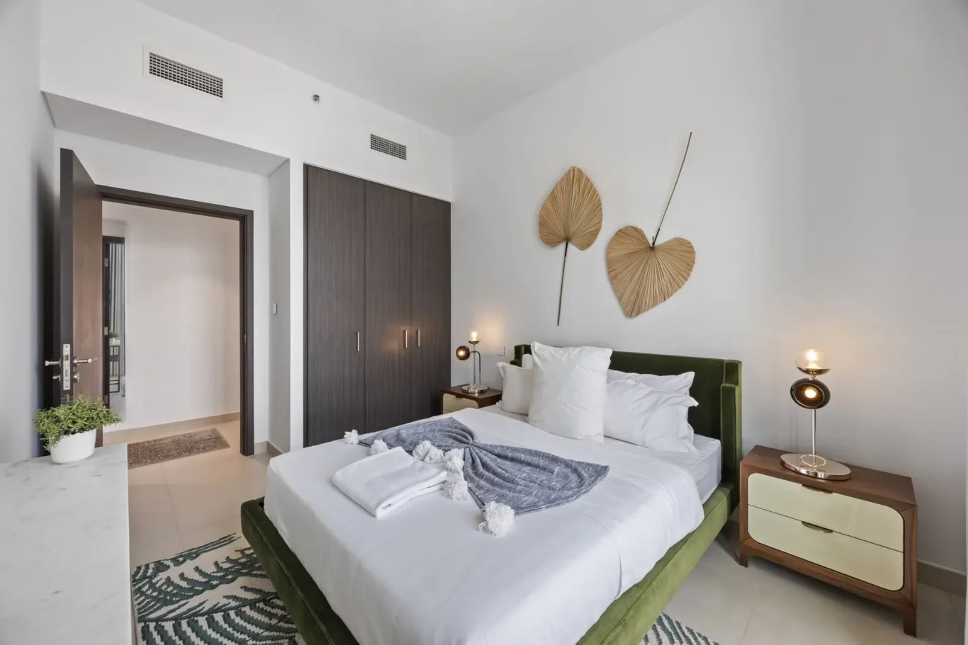 Modern bedroom with a green upholstered bed, white bedding, and palm-leaf wall art above the headboard.