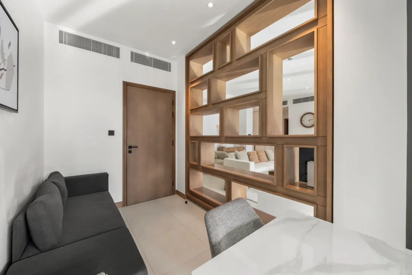 Modern living area with a dark gray sofa, a wooden door, and a large open-shelved wooden partition separating spaces.