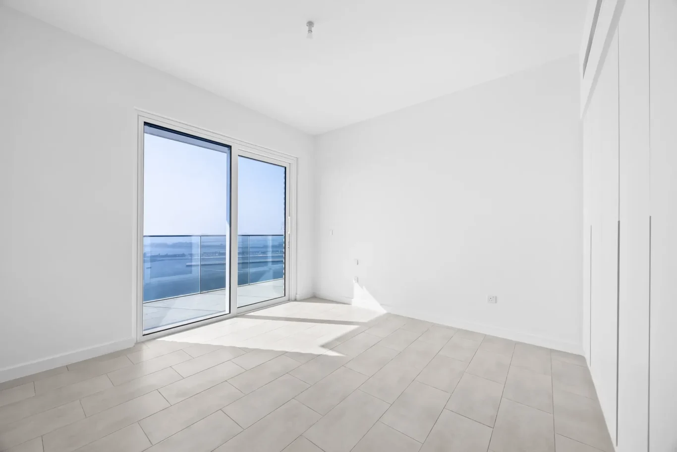 Bright empty white room with large sliding glass doors opening to a balcony and an ocean view.