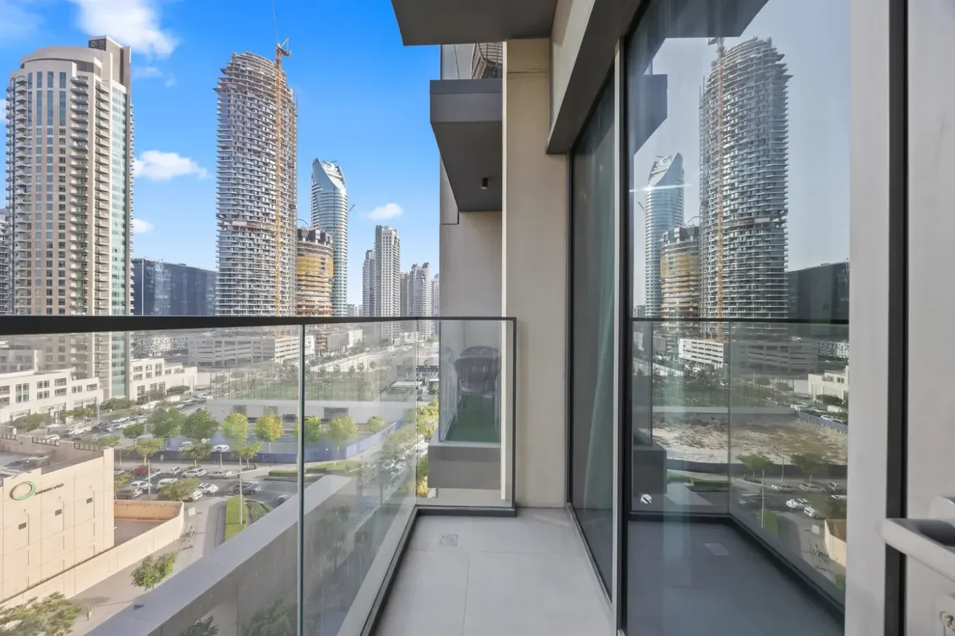 Balcony of a modern high-rise with glass railing, overlooking a city skyline of skyscrapers under construction against a blue sky.