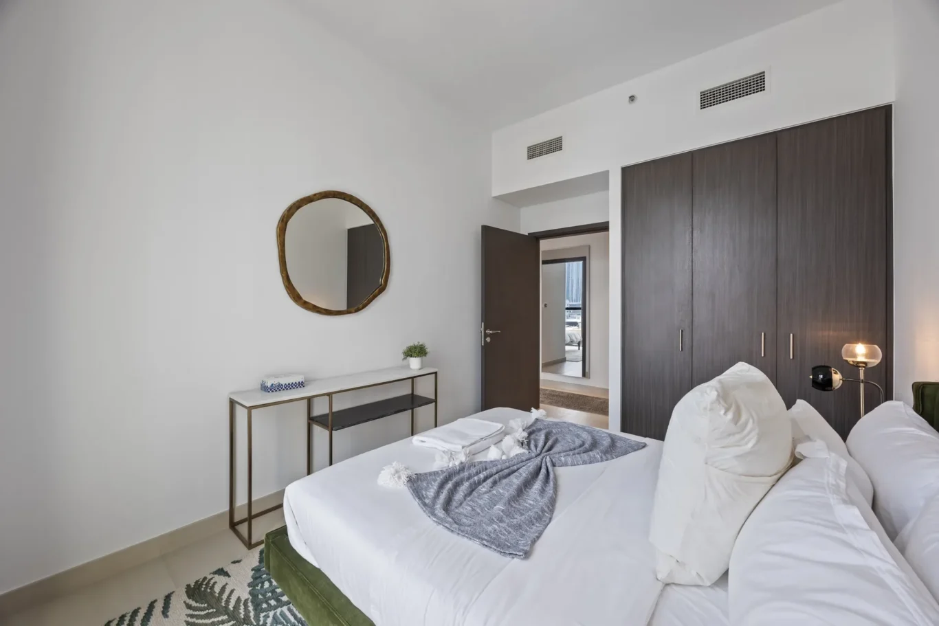 Twin beds with white linens and gray throws in a modern hotel room, wood wardrobe along the wall.