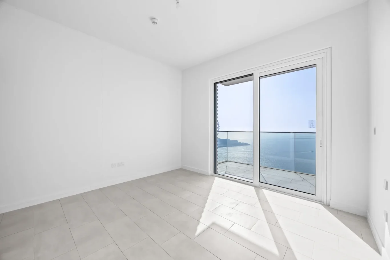 Empty bright room with large glass sliding doors opening to a balcony and sea view. (informative)