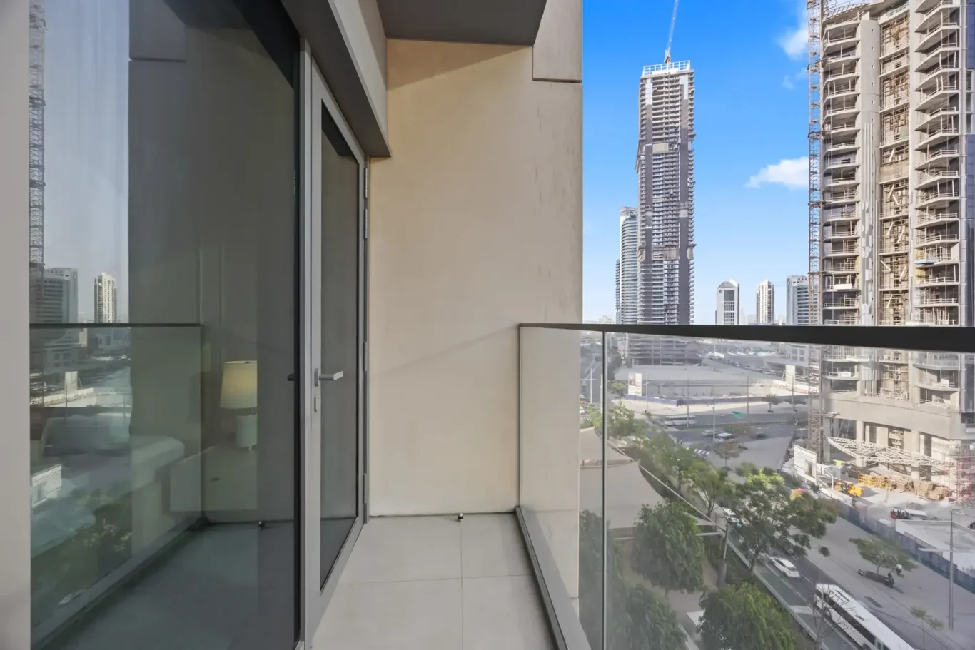 Balcony with glass railing overlooking a city street and tall buildings under construction in clear weather.