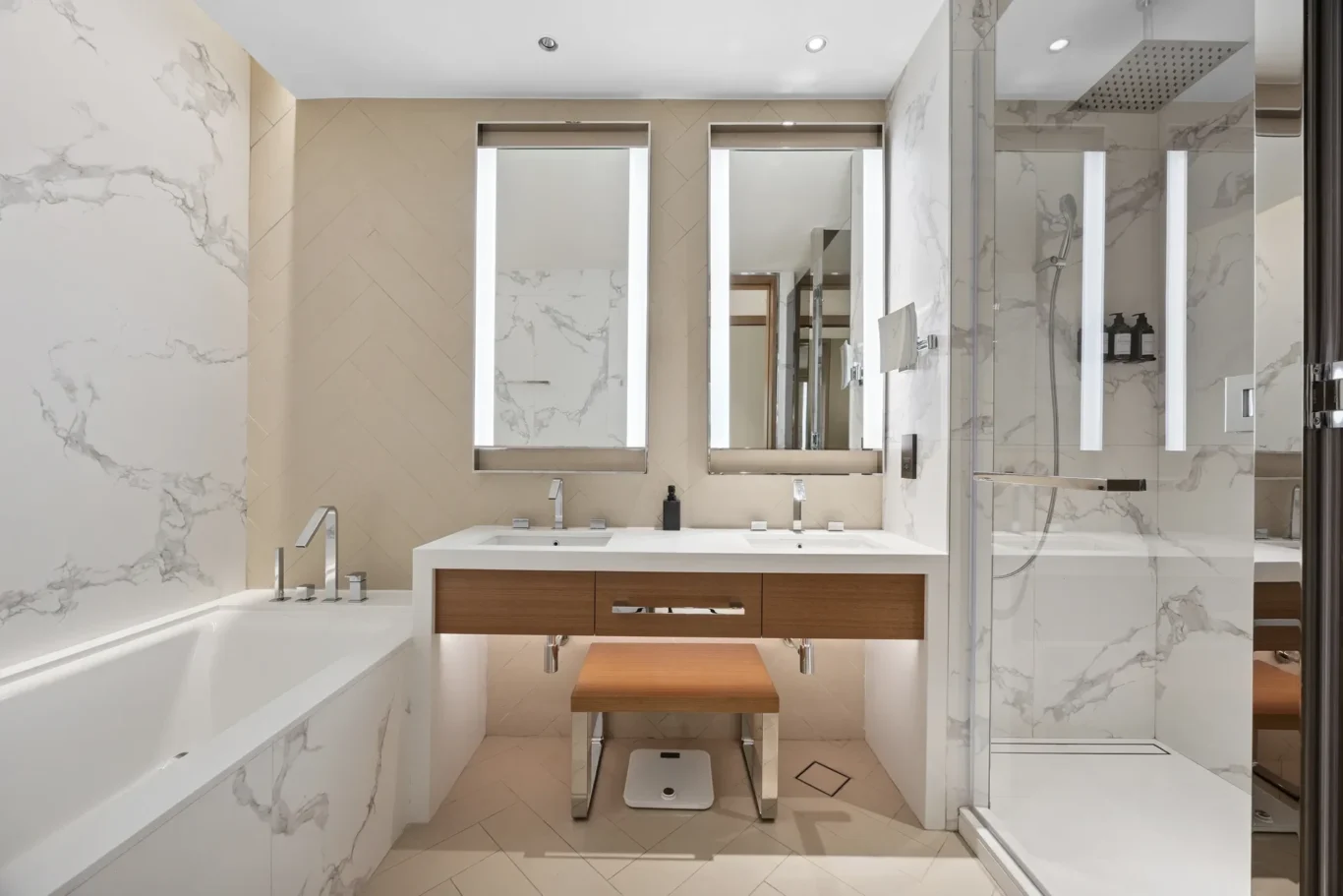 Modern bathroom with a white double vanity, wood drawers, and two mirrors flanked by vertical lights; marble walls and a glass shower.