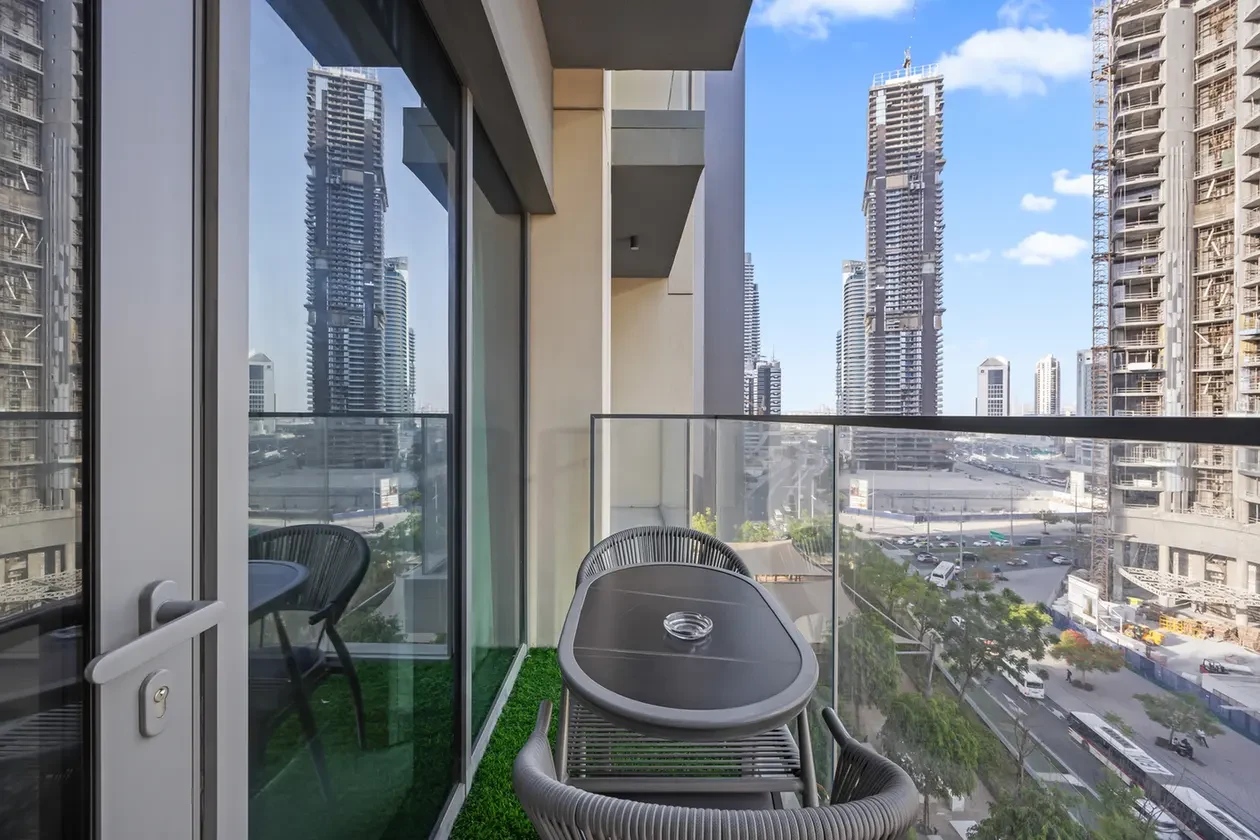 Balcony with glass railing overlooking a city street and tall skyscrapers under a blue sky.