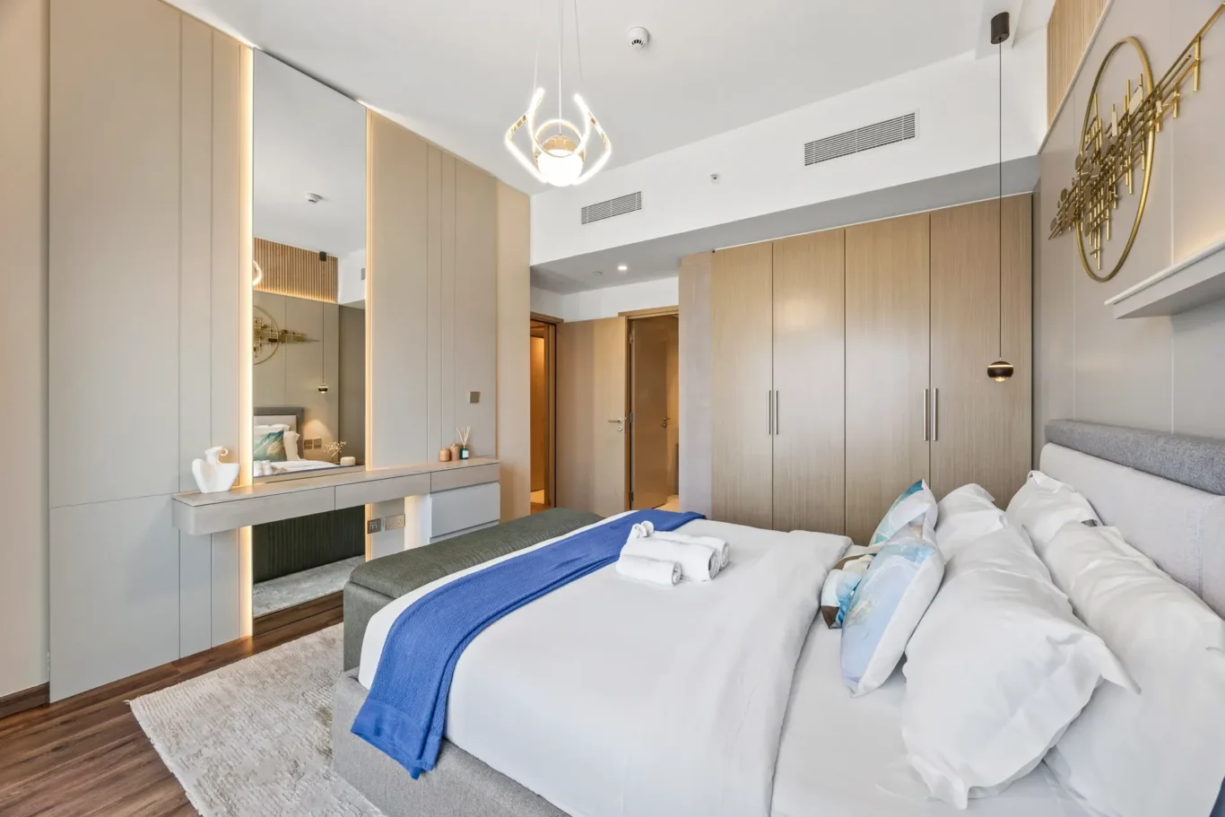 Twin-bed hotel room with white bedding and blue runners, built-in beige wardrobes, and a spacious vanity area with mirror.