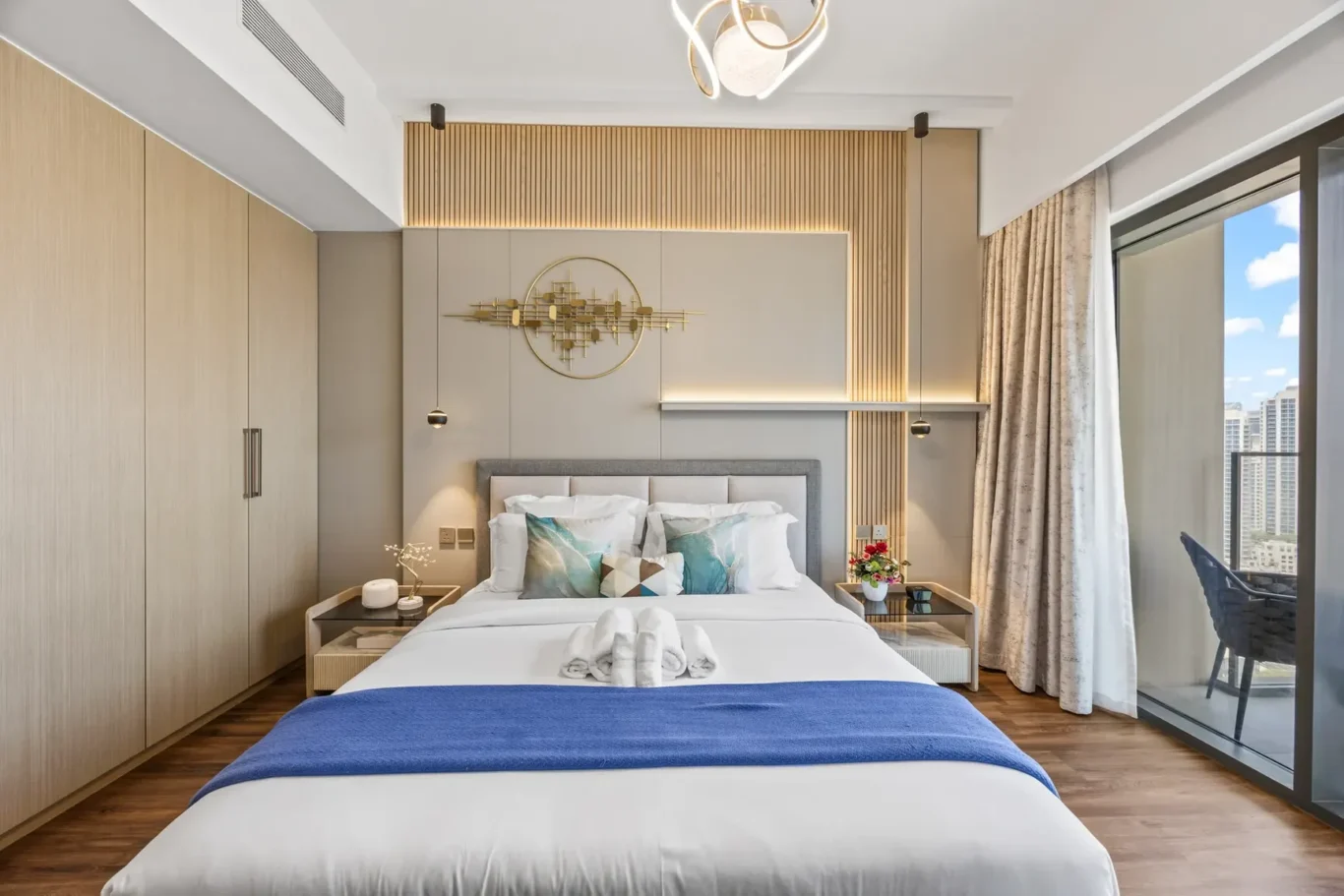 Modern hotel bedroom with a large bed, gray headboard, and warm wood-paneled accent wall facing a balcony with city views