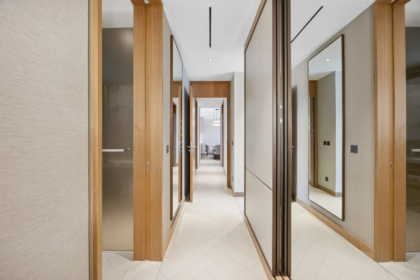 Long, bright hallway with wooden door frames and full-length mirrors on the right, leading to a seating area at the end.
