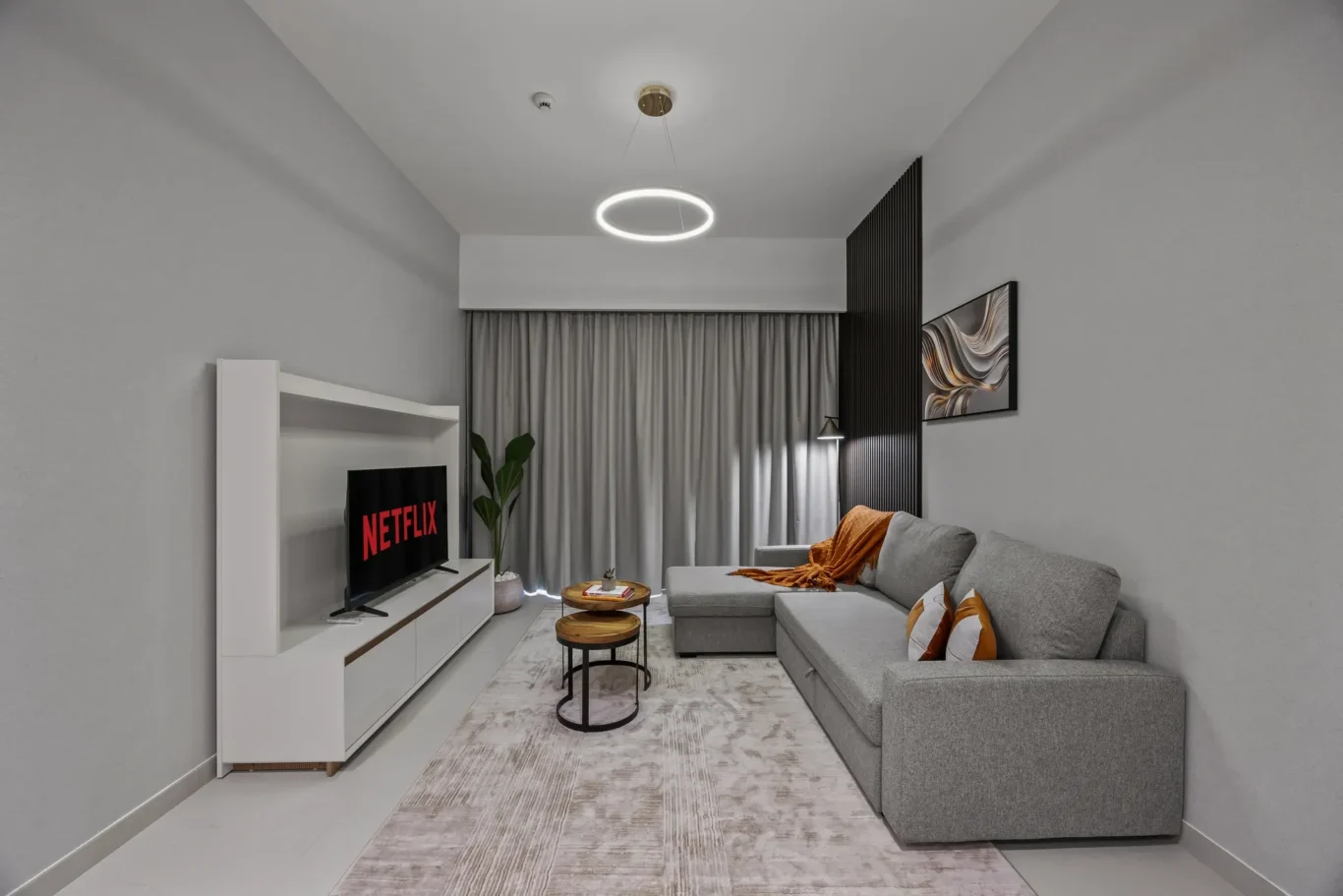Modern living room with grey walls, white media unit, and a grey sectional sofa facing a Netflix TV screen.