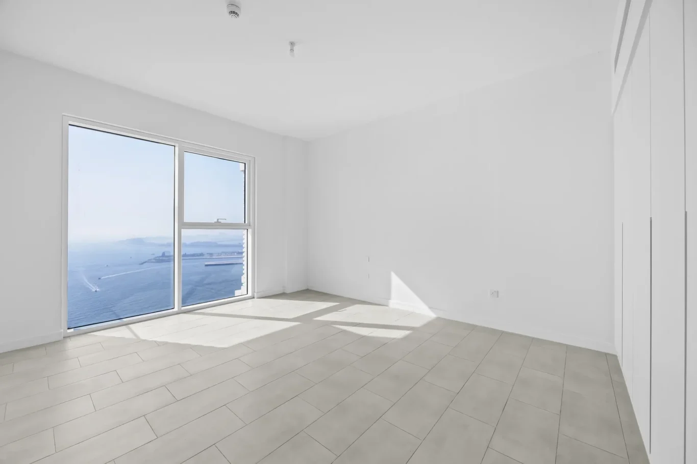 Empty white room with large sliding glass doors showing the ocean beyond the coastline.