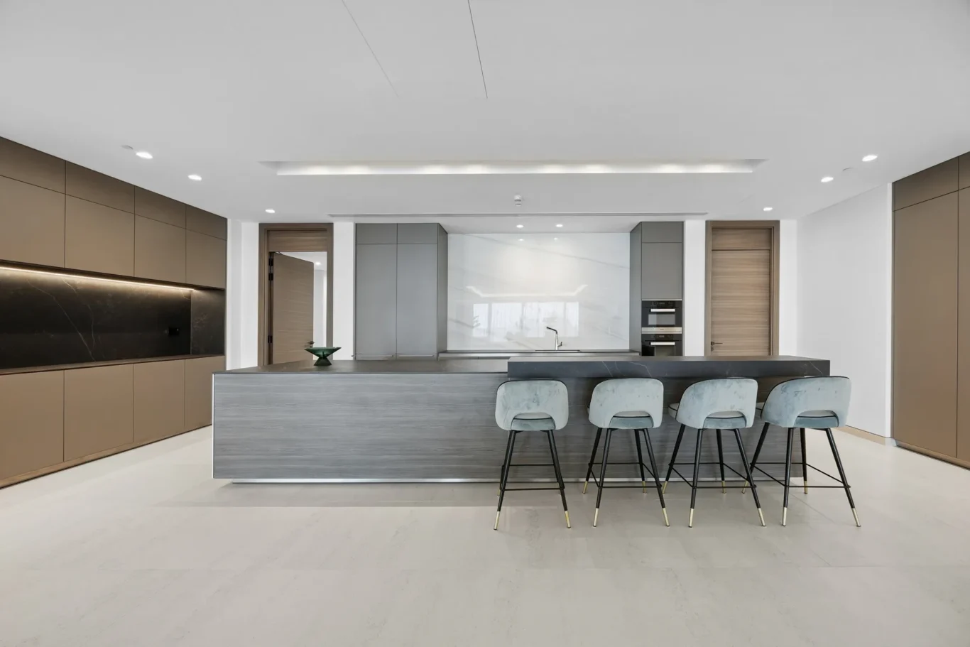 Modern kitchen with a large two-tone island, grey wood-grain panels, and light blue bar stools lined along the counter.